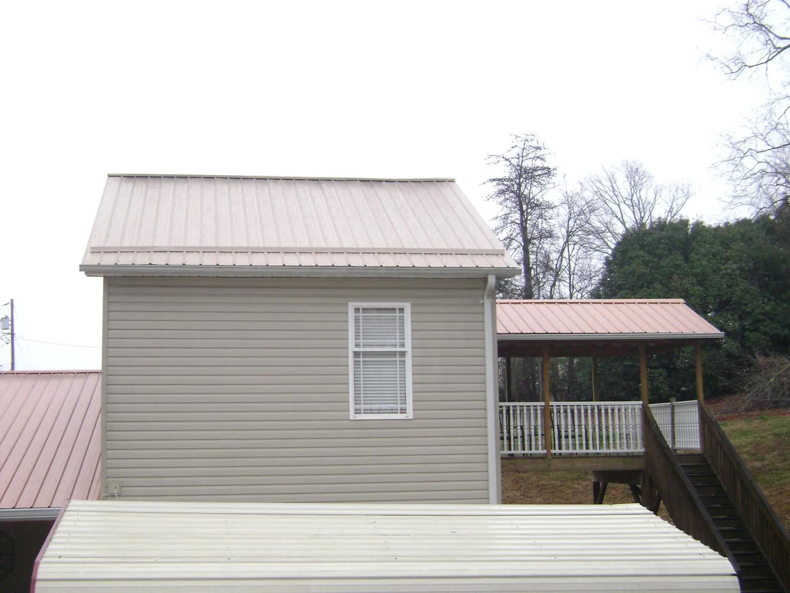 Tan metal roofs on a two story addition and attached porch, from a Roof Replacement job in Monroe